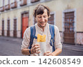 Man traveler holding a golden molote poblano traditional fried Mexican empanada outdoors on a street in Puebla Mexico with colonial city background paper wrapper local street food authentic travel. 142608549