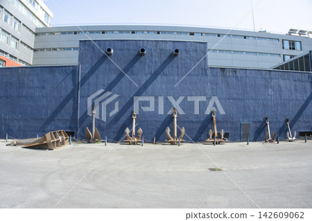Row of old ship anchors displayed against a deep blue concrete wall Row of old ship anchors displayed against a deep blue concrete wall 142609062