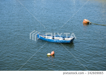 Old blue wooden rowing boat moored between buoys on calm harbour water Old blue wooden rowing boat moored between buoys on calm harbour water 142609065