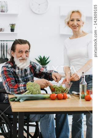 An elderly couple happily prepares a fresh salad in their bright, modern kitchen, showcasing teamwork and healthy living An elderly couple happily prepares a fresh salad in their bright, modern kitchen, showcasing teamwork and healthy living 142609105