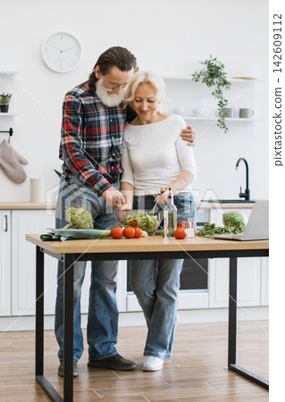 An elderly couple lovingly prepares a fresh salad in their bright, modern kitchen, showcasing a healthy lifestyle and shared activity An elderly couple lovingly prepares a fresh salad in their bright, modern kitchen, showcasing a healthy lifestyle and shared activity 142609112