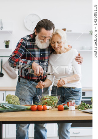 An elderly couple happily prepares a fresh salad in a bright, modern kitchen, showcasing a healthy lifestyle and shared activity An elderly couple happily prepares a fresh salad in a bright, modern kitchen, showcasing a healthy lifestyle and shared activity 142609119