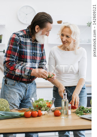 An elderly couple happily prepares a fresh salad and other vegetables in a bright, modern kitchen, showcasing healthy lifestyle choices An elderly couple happily prepares a fresh salad and other vegetables in a bright, modern kitchen, showcasing healthy lifestyle choices 142609121