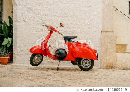 Classic Vespa scooter stands beside a limestone wall in Locorotondo, Italy. The image reflects freedom, heritage, mobility and Mediterranean lifestyle Classic Vespa scooter stands beside a limestone wall in Locorotondo, Italy. The image reflects freedom, heritage, mobility and Mediterranean lifestyle 142609349