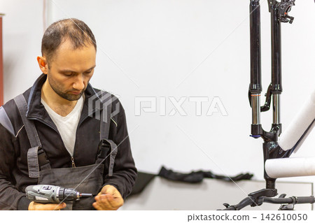 Mechanic using a cordless drill to assemble black bicycle fork parts Mechanic using a cordless drill to assemble black bicycle fork parts 142610050