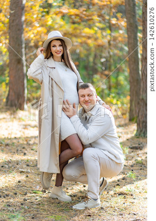 A happy couple poses in a forest during the fall season, celebrating their pregnancy A happy couple poses in a forest during the fall season, celebrating their pregnancy 142610276