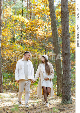 A pregnant woman and her partner stroll hand-in-hand through a sun-dappled forest, enjoying the fall colors A pregnant woman and her partner stroll hand-in-hand through a sun-dappled forest, enjoying the fall colors 142610302