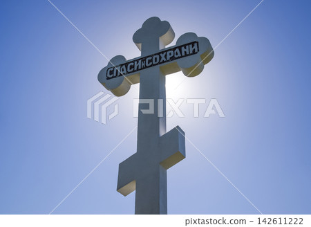 Orthodox cross against the blue sky and the sun. Cross in the backlight of the sun. Symbol of the Christian faith. The inscription on the cross: salvation and preservation Orthodox cross against the blue sky and the sun. Cross in the backlight of the sun. Symbol of the Christian faith. The inscription on the cross: salvation and preservation 142611222