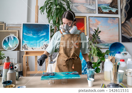 Female artist shaping fluid epoxy resin with wooden spatula to create pattern on abstract painting. Female artist shaping fluid epoxy resin with wooden spatula to create pattern on abstract painting. 142611531