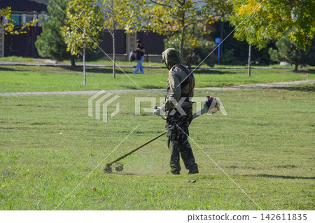 worker mowing grass with a gasoline brush. Trimmer. worker mowing grass with a gasoline brush. Trimmer. 142611835