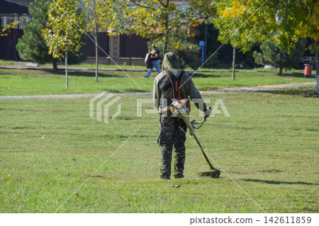 worker mowing grass with a gasoline brush. Trimmer. 142611859