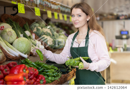 Woman employees in uniform holding fresh bell pepper in grocery shop Woman employees in uniform holding fresh bell pepper in grocery shop 142612064