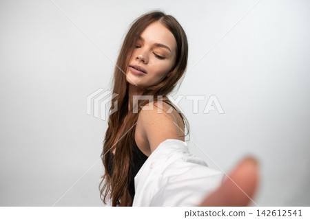 Young woman with closed eyes pulling a white shirt on her shoulder with long brown hair casual portrait Young woman with closed eyes pulling a white shirt on her shoulder with long brown hair casual portrait 142612541