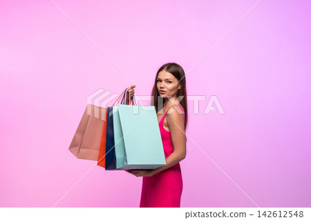 Young woman enjoying retail therapy, carrying colorful shopping bags on a vibrant pink background Young woman enjoying retail therapy, carrying colorful shopping bags on a vibrant pink background 142612548