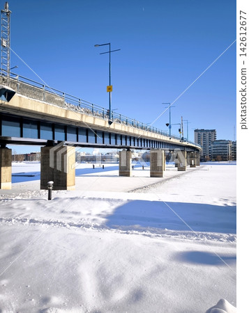 A view from below of bridge supports and a frozen, snow-covered river on a clear, frosty day. A view from below of bridge supports and a frozen, snow-covered river on a clear, frosty day. 142612677