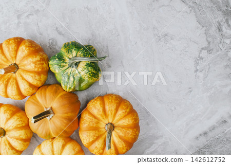 Mini decorative pumpkins in various shades of orange and green arranged on a textured gray surface, ideal for Halloween and autumn-themed decorations or seasonal displays Mini decorative pumpkins in various shades of orange and green arranged on a textured gray surface, ideal for Halloween and autumn-themed decorations or seasonal displays 142612752
