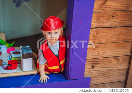 Little boy dressed as firefighter playing in a red toy fire truck at an outdoor playground with helmet safety vest pretend rescue game childhood dreams role play and rear view. Little boy dressed as firefighter playing in a red toy fire truck at an outdoor playground with helmet safety vest pretend rescue game childhood dreams role play and rear view. 142612905