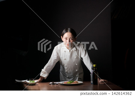 一位女廚師一邊擺放菜餚一邊微笑。 一位女廚師一邊擺放菜餚一邊微笑。 142614362