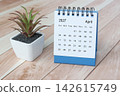 April 2027 desk calendar with potted plant on wooden desk. 142615749