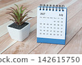 July 2027 desk calendar with potted plant on wooden desk. 142615750