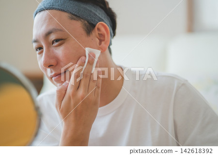 一位四十多歲的男子在鏡子前,用化妝棉蘸取大量潤膚露輕拍臉部,這是他日常男士美容程序的一部分。 一位四十多歲的男子在鏡子前,用化妝棉蘸取大量潤膚露輕拍臉部,這是他日常男士美容程序的一部分。 142618392