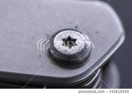 Extreme close up of worn metal Torx screw head fastened into dark mechanical component showing industrial hardware texture engineering detail maintenance concept Extreme close up of worn metal Torx screw head fastened into dark mechanical component showing industrial hardware texture engineering detail maintenance concept 142618450