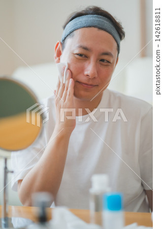A 40-year-old man's beauty routine: applying lotion to his cheeks with a cotton pad while looking in the mirror. A 40-year-old man's beauty routine: applying lotion to his cheeks with a cotton pad while looking in the mirror. 142618811