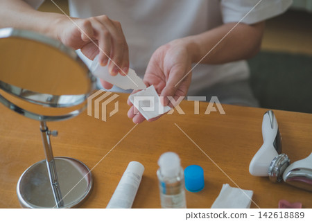 一位四十多歲的男士整理他的化妝品,並將乳液塗抹在化妝棉上,這是他男士護膚程序的一部分。 一位四十多歲的男士整理他的化妝品,並將乳液塗抹在化妝棉上,這是他男士護膚程序的一部分。 142618889