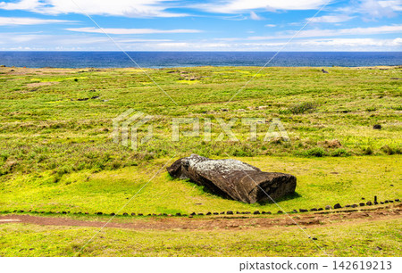 A fallen stone Moai statue lies on the grassy slopes of Rano Raraku with the blue ocean in the background on Easter Island, Chile. A fallen stone Moai statue lies on the grassy slopes of Rano Raraku with the blue ocean in the background on Easter Island, Chile. 142619213