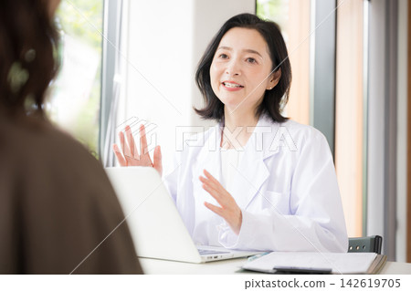在診所的畫面中,一位女醫師面帶微笑地面對病人,提供醫療諮詢、檢查和健康諮詢。 在診所的畫面中,一位女醫師面帶微笑地面對病人,提供醫療諮詢、檢查和健康諮詢。 142619705