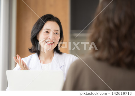 The image of a clinic where a female doctor faces patients and provides medical counseling, examinations, and health consultations with a smile. The image of a clinic where a female doctor faces patients and provides medical counseling, examinations, and health consultations with a smile. 142619713