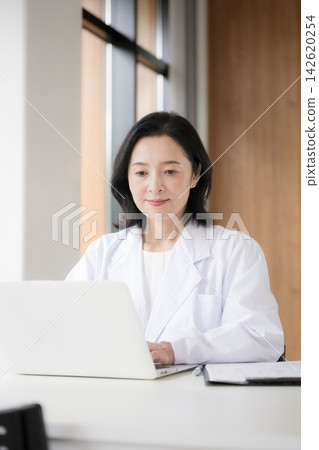 醫療諮詢中的一個場景,一位女醫生正在電腦上將病人資訊和醫療記錄輸入電子病歷系統。 醫療諮詢中的一個場景,一位女醫生正在電腦上將病人資訊和醫療記錄輸入電子病歷系統。 142620254