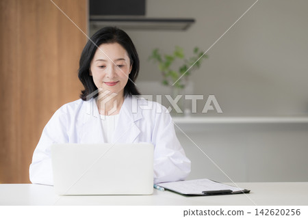 醫療諮詢中的一個場景，一位女醫生正在電腦上將病人資訊和醫療記錄輸入電子病歷系統。 142620256