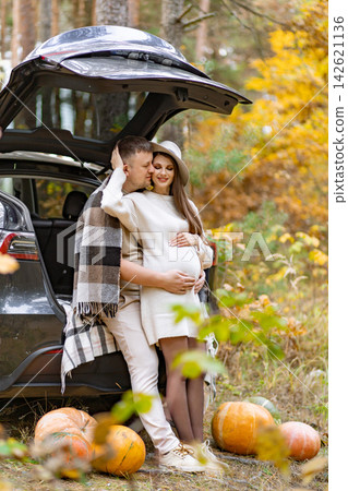 A loving couple embraces in a forest setting, celebrating their pregnancy with pumpkins and a car 142621136
