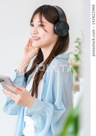 一位年輕女性的數位生活:用耳機和智慧型手機享受音樂和音訊內容。 一位年輕女性的數位生活:用耳機和智慧型手機享受音樂和音訊內容。 142622966