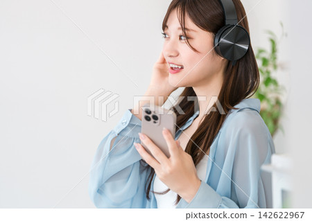 一位年輕女性的數位生活:用耳機和智慧型手機享受音樂和音訊內容。 一位年輕女性的數位生活:用耳機和智慧型手機享受音樂和音訊內容。 142622967