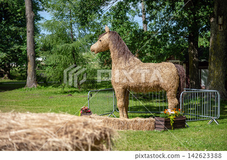 Straw horse sculpture stands in a park surrounded by trees during sunny daytime Straw horse sculpture stands in a park surrounded by trees during sunny daytime 142623388