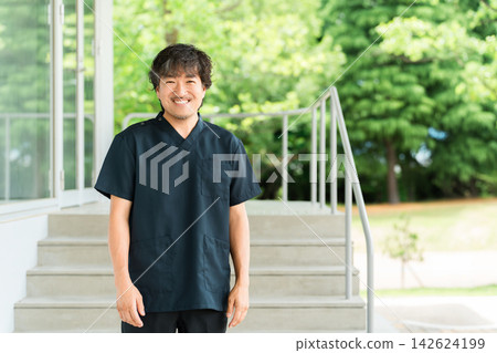 一名男性物理治療師和其他復健醫學專業人員面帶微笑地站在綠色背景前。 142624199