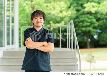 A male doctor, surgeon, or specialist in scrubs, with his arms crossed and a smile on his face. 142624201