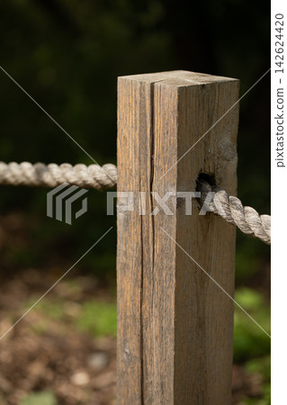 Weathered, textured rustic wooden fence post with thick rope on a blurred natural green background Weathered, textured rustic wooden fence post with thick rope on a blurred natural green background 142624420
