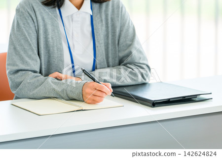 A female staff member's hands taking notes while listening during training sessions and interviews. A female staff member's hands taking notes while listening during training sessions and interviews. 142624824