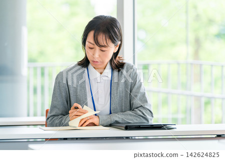 A female staff member reviews her work while checking her notes - a scene where she reviews training and work records. A female staff member reviews her work while checking her notes - a scene where she reviews training and work records. 142624825