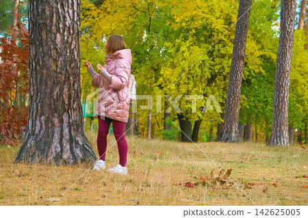 Nice woman in pink jacket and red jeans near pine tree in an autumn park Nice woman in pink jacket and red jeans near pine tree in an autumn park 142625005