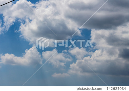 A dramatic view of thick clouds and blue sky with the silhouette of power lines running across the upper left - from a low angle. A dramatic view of thick clouds and blue sky with the silhouette of power lines running across the upper left - from a low angle. 142625084