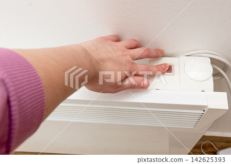 Woman presses button to turn on electric battery, heating in winter in Europe Woman presses button to turn on electric battery, heating in winter in Europe 142625393