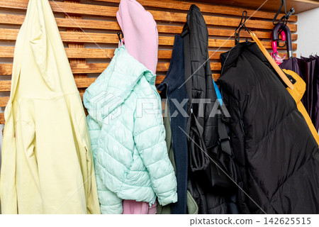 Autumn outerwear jacket and coat on hangers in wooden wardrobe shelf in hallway Autumn outerwear jacket and coat on hangers in wooden wardrobe shelf in hallway 142625515