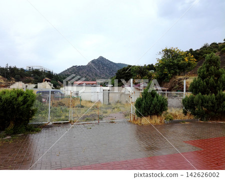 fenced lot with buildings at foot of mountain under grey sky fenced lot with buildings at foot of mountain under grey sky 142626002