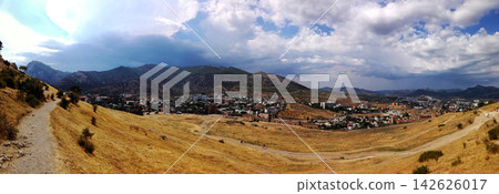 panorama of a valley with a town, mountain range, dirt path and dramatic clouds in sky panorama of a valley with a town, mountain range, dirt path and dramatic clouds in sky 142626017