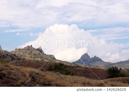 picturesque hilly landscape with a sharp rocky peak against puffy cumulus clouds in the sky 142626029