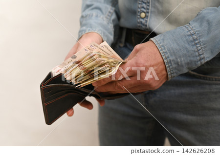 Hand holds open wallet overflowing with crisp banknotes. Hand holds open wallet overflowing with crisp banknotes. 142626208